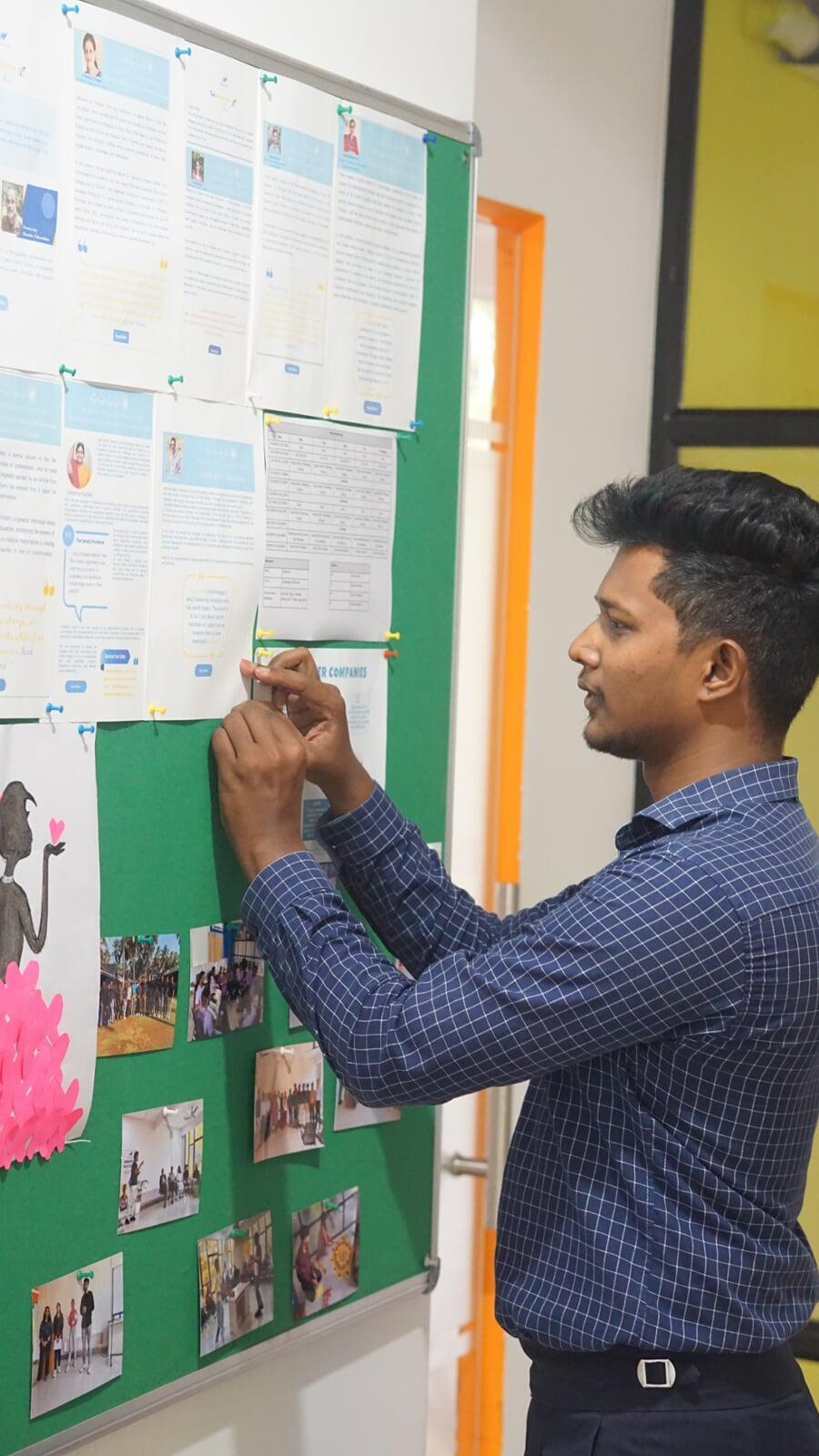 Employee curating Tekvocation’s workplace bulletin board with team updates, creative contributions, and workshop visuals